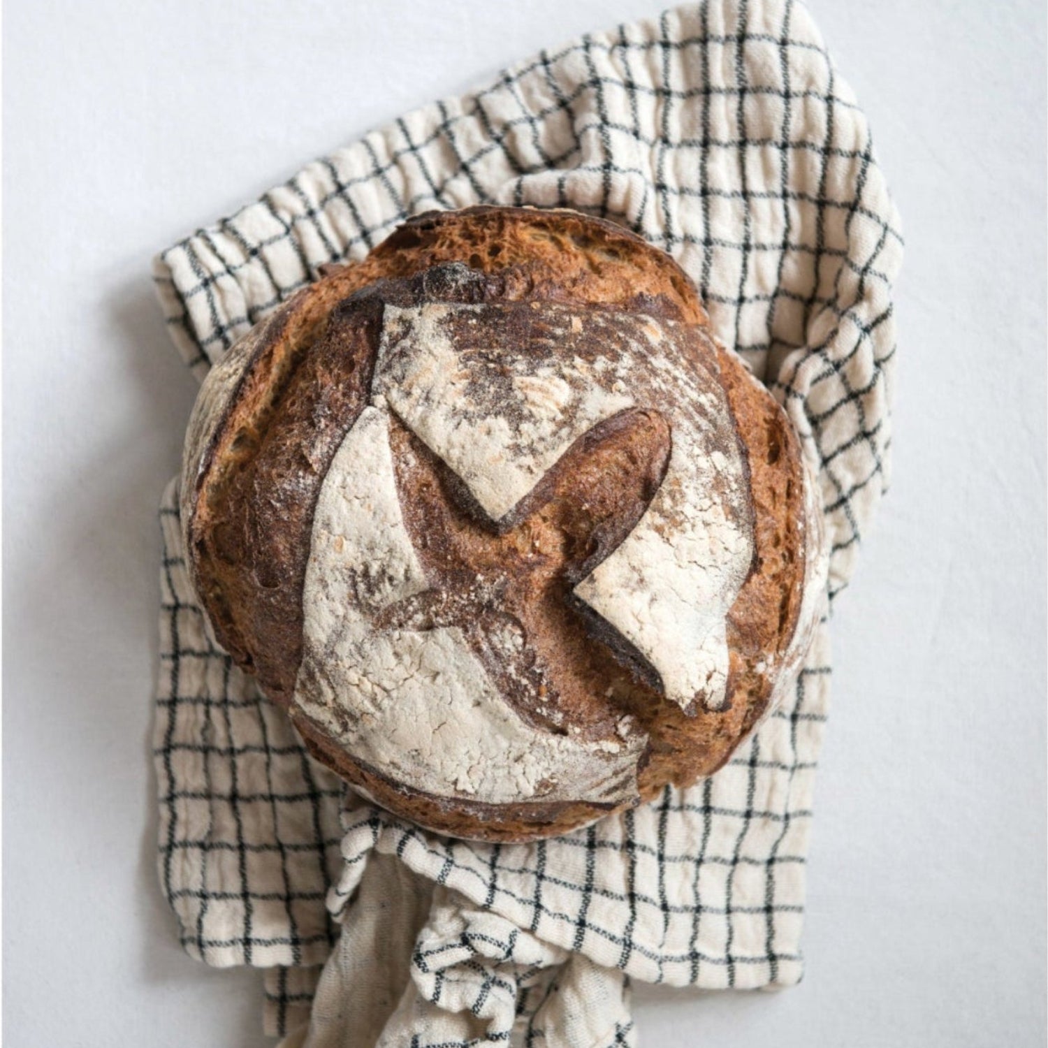 Loaf of bread on a checkered cloth with a light gray background