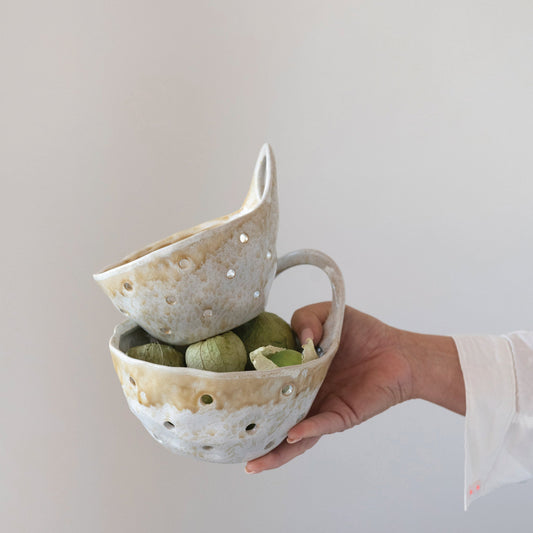 Hand holding a straining ceramic bowl with another bowl inside on a plain background