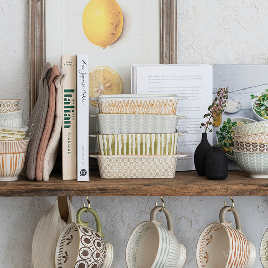 Decorative shelf with patterned bowls, books, and hanging mugs against a light wall.
